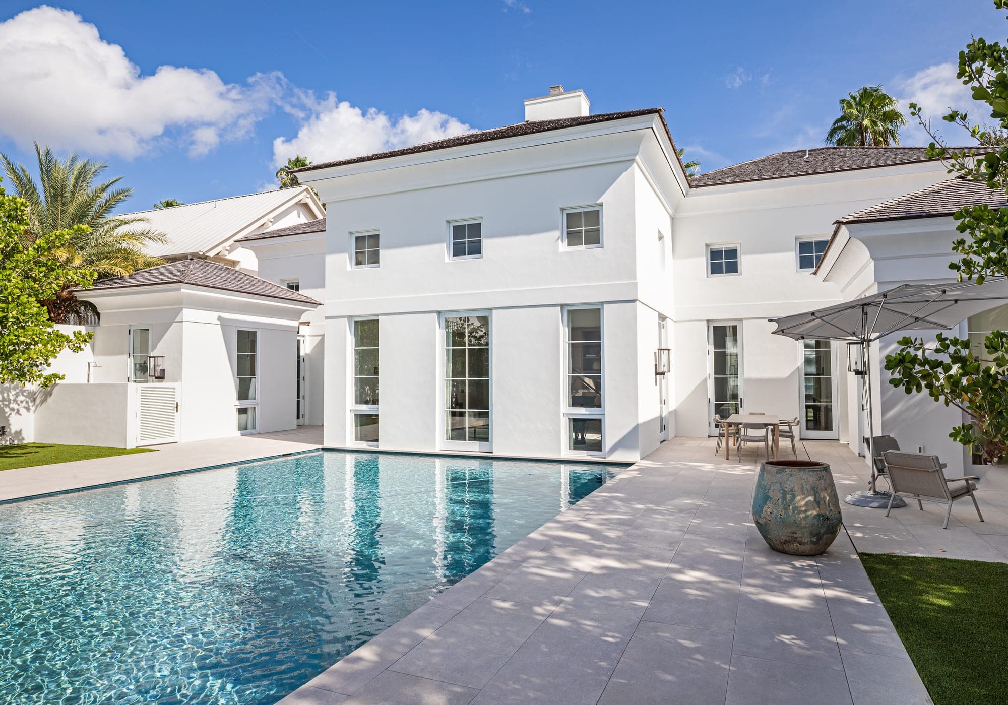 Pool terrace behind a two-story white residence in Windsor & North Island, Vero Beach by Builders East